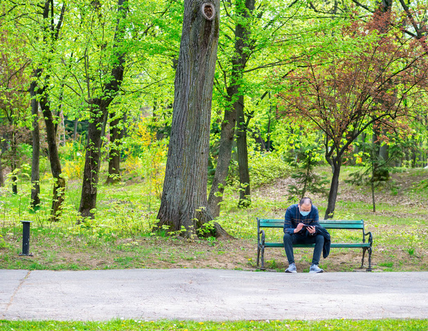 Bucharest, Romania - 04.15.2022: Single isolated man sitting on a bench in King Mihai I park (Herestrau) - Photo, image
