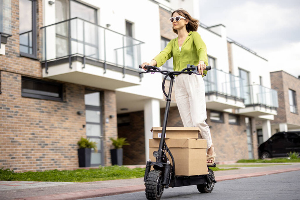 Woman driving electric scooter with cardboard packages - Foto, immagini