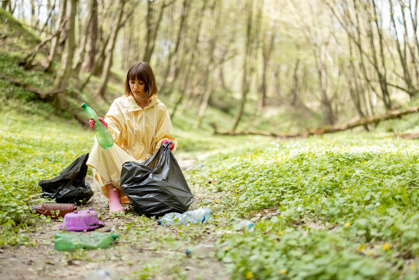 Woman collecting scattered plastic garbage in the woods - Foto, Bild