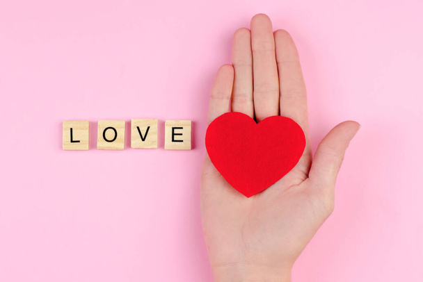 Word love from wooden letters and a heart on a female hand, selective focus - Foto, Imagen