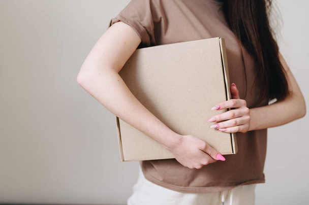 A close-up female hand holds a cardboard box, in a brown-beige color scheme. cropped frame - Fotó, kép