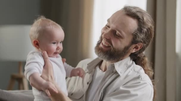 Yakın plan mutlu baba şefkatli orta yaşlı baba sakallı adam küçük kızı tutuyor çocuk zıplıyor erkek ebeveyn gülerek evde bebek bakıcılığı yapan yeni doğmuş bebekle vakit geçiriyor. - Video, Çekim