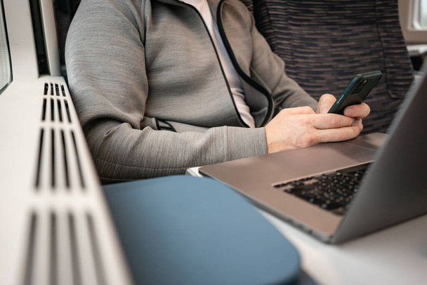 A male businessman works sitting on a train on the road using a phone and laptop. Travel in Europe by train. Remote work, digital nomad - Foto, Imagen