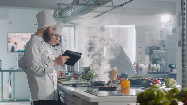 Team von Köchen bereitet mit digitalem Tablet authentisches Gourmet-Menü zu - Foto, Bild