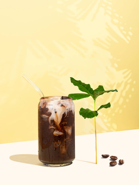Robusta boisson de café glacé, grains de café et feuilles sur un fond jaune. Coupe en verre en forme de boîte de café avec du lait non laitier. Paille à boire réutilisable. Concept d'alimentation et de boissons durables. - Photo, image