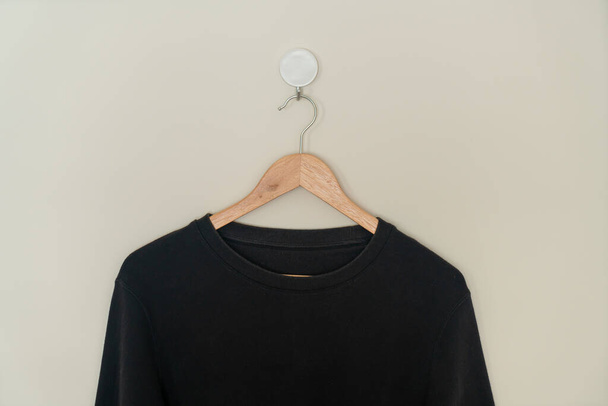 black sweater hanging with wood hanger on wall - Foto, immagini