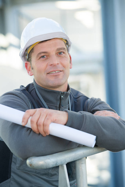 worker holding rolled blueprint posing and smiling - Fotó, kép