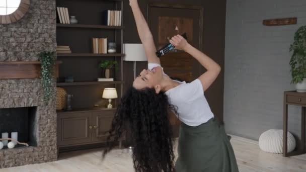 Νεαρή ελκυστική ενεργή γυναίκα αστεία χοροί δυναμική στο σύγχρονο σαλόνι ακούει μουσική τραγουδά αγαπημένο τραγούδι χρησιμοποιεί τηλεχειριστήριο ως μικρόφωνο ξέγνοιαστη νοικοκυρά απολαμβάνει το Σαββατοκύριακο την ανεξαρτησία - Πλάνα, βίντεο
