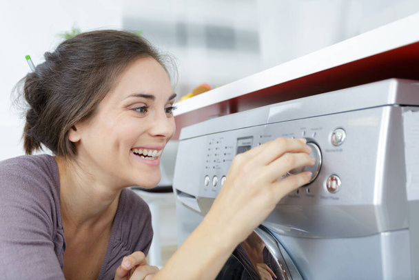 young brunette doing laundry in kitchen and smiling - Foto, Bild