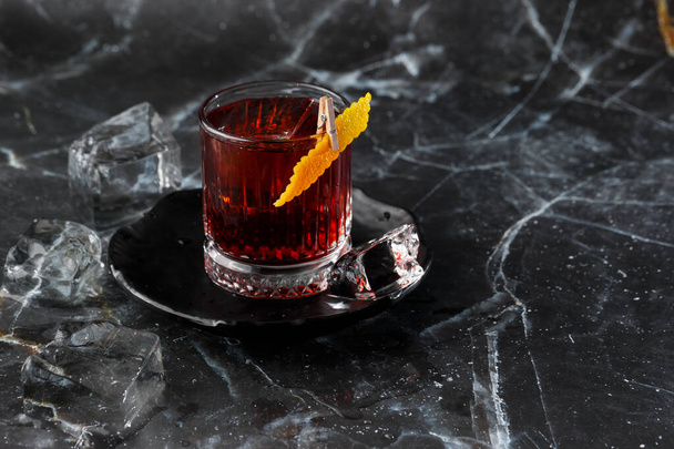 Crystal glass with bright cold alcoholic cocktail decorated with orange zest. Blurred background. Negroni cocktail - Фото, изображение