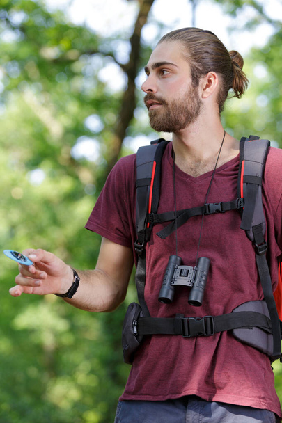male hiker looking through binoculars in forest - Zdjęcie, obraz