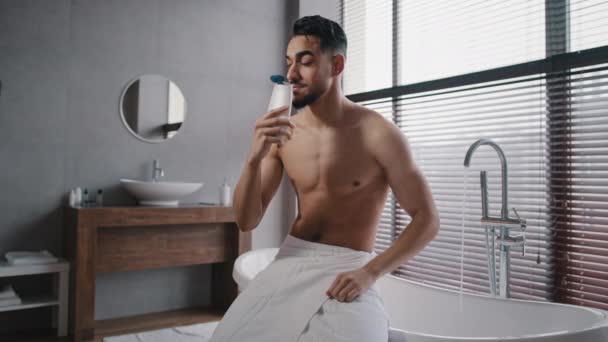 Arabisch indiaan man gespierd naakt sexy ongeschoren man draagt witte badhanddoek op heupen zit in de badkamer klaar voor het baden wassen snuiven douchegel ochtend verfrissing met natuurlijke mannelijke cosmetica - Video
