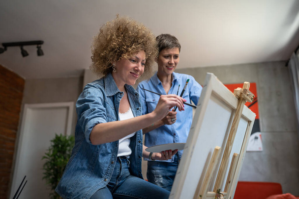 Dwie kobiety przyjaciółki lub kobieta ze swoim mentorem sztuki profesor kaukaskie dojrzałe siostry uczą i dowiedzieć się, jak malować pomagając podczas malowania nie sztalugi w domu w jasnym pokoju skopiować przestrzeń - Zdjęcie, obraz