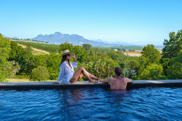 Yüzme havuzundaki çift, Güney Afrika 'nın üzüm bağlarına ve dağlarına bakıyor. - Fotoğraf, Görsel