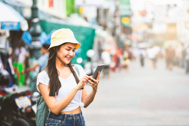 Joven viajero asiático mujer feliz en camisa blanca con mochila. Uso de la comunidad de búsqueda de teléfonos inteligentes. Junto a la histórica calle Khaosan. Bangkok City, Tailandia - Foto, imagen