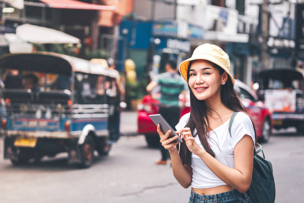 Joven adulto asiático viajero feliz mujer con mochila. Visitas turísticas en solitario. Ella usa el teléfono inteligente para el transporte y reserva de hotel. Estilo de vida moderno digital. En la calle comercial Khaosan. Bangkok, Tailandia - Foto, imagen