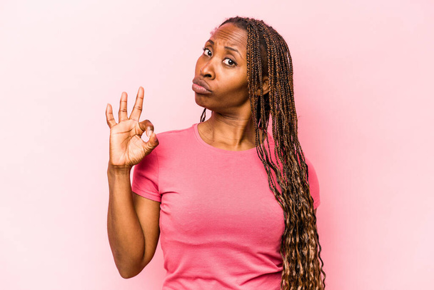 Nuori afrikkalainen amerikkalainen nainen eristetty vaaleanpunainen tausta iskee silmää ja pitää kunnossa ele käsin. - Valokuva, kuva