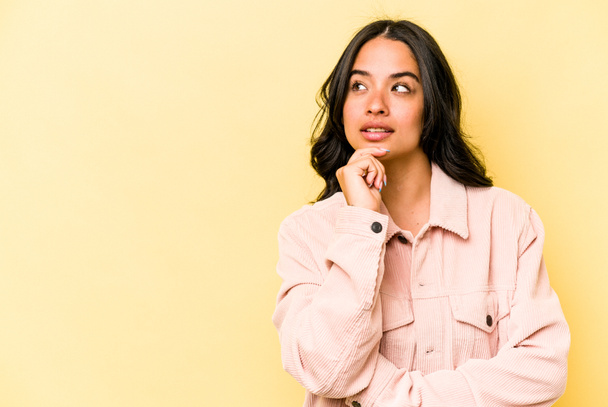 Young hispanic woman isolated on yellow background looking sideways with doubtful and skeptical expression. - Фото, зображення