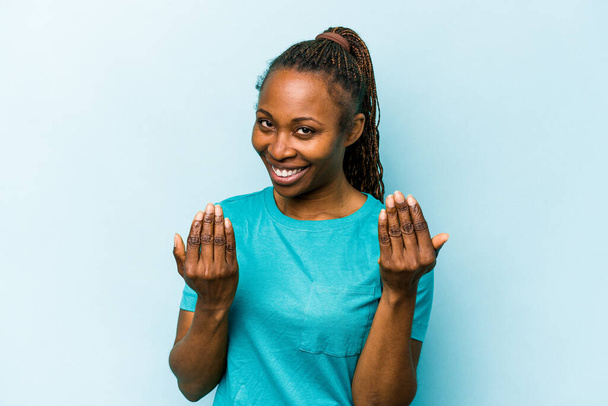 Young african american woman isolated on blue background pointing with finger at you as if inviting come closer. - Foto, Imagem