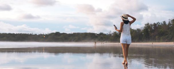 Придивіться до молодої дорослої туристичної жінки, яка ходить, відпочиваючи на пляжному піску з прекрасним драматичним заходом сонця. Внутрішня подорож в океан андамана. Пхукет, Таїланд. - Фото, зображення