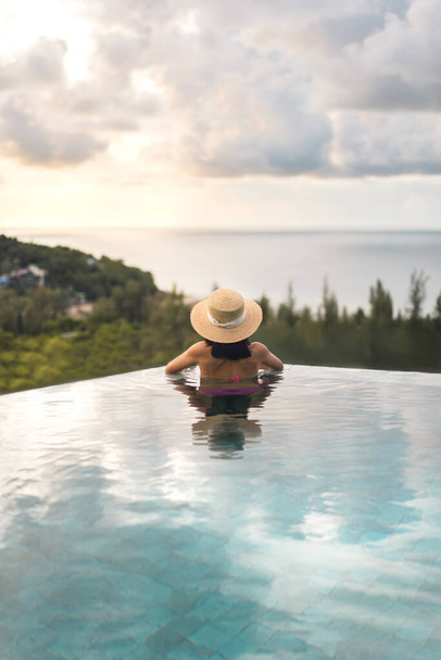 Letnie podróże na wakacje w południowo-wschodniej koncepcji tropikalnej. Widok z tyłu Azja kobieta relaks w odkryty basen kurort widok na morze panorama. Ze słomkowym kapeluszem i dramatycznym niebem. Wyspa Phuket, Tajlandia - Zdjęcie, obraz
