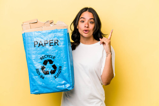 Jovem mulher hispânica reciclagem de papel isolado no fundo amarelo tendo alguma grande ideia, conceito de criatividade. - Foto, Imagem