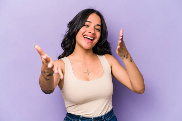 Young hispanic woman isolated on purple background feels confident giving a hug to the camera. - 写真・画像