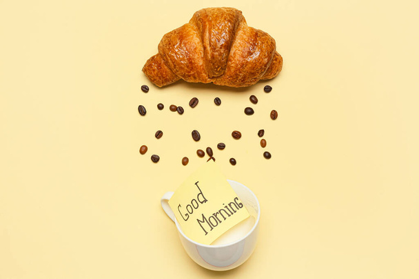 Krásná kompozice s croissant, kávová zrna, pohár a lepkavý tón s textem Dobré ráno na barevném pozadí - Fotografie, Obrázek