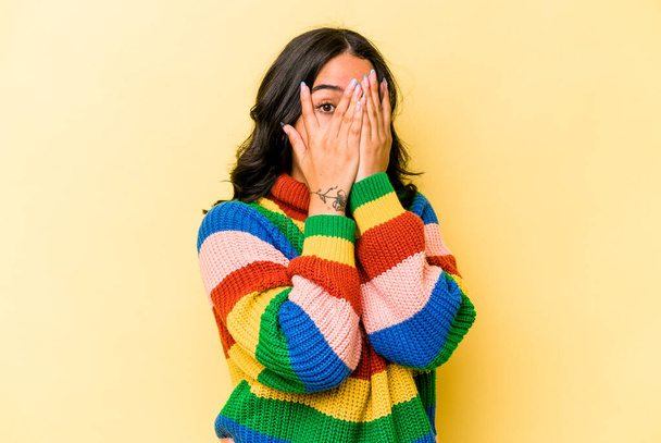 Young hispanic woman isolated on yellow background blink through fingers frightened and nervous. - Фото, изображение