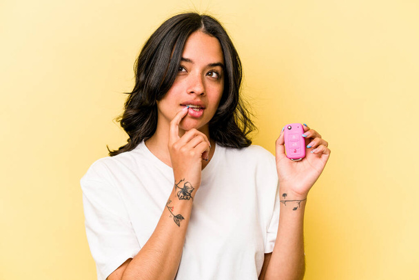 Young hispanic woman holding a keys car isolated on pink background relaxed thinking about something looking at a copy space. - Foto, immagini