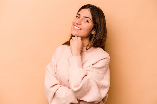 Young hispanic woman isolated on beige background smiling happy and confident, touching chin with hand. - Φωτογραφία, εικόνα