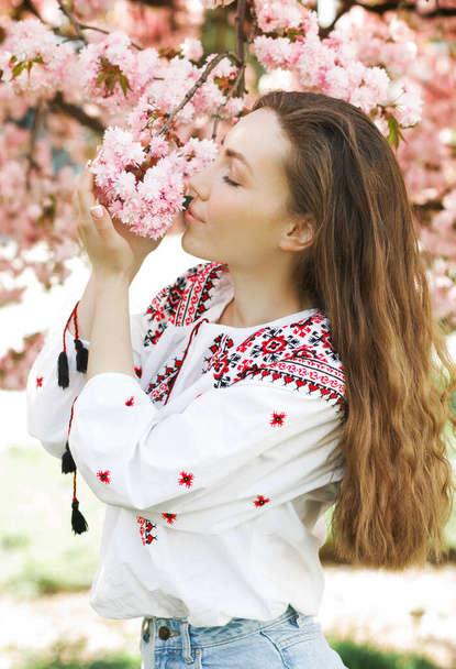 Portrait of a ukrainian woman in an embroidered shirt near the blossoming sakura in the park - Foto, Imagem