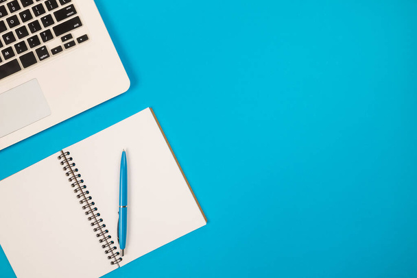 Фото ручки с блокнотом и ноутбуком на изолированном синем фоне с копировальным пространством - Фото, изображение