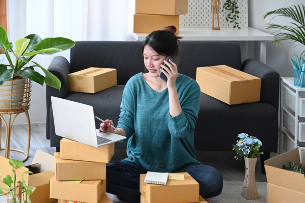 Startup small business entrepreneur receive order on mobile phone and using laptop at home. E-commerce, Online selling concept - 写真・画像