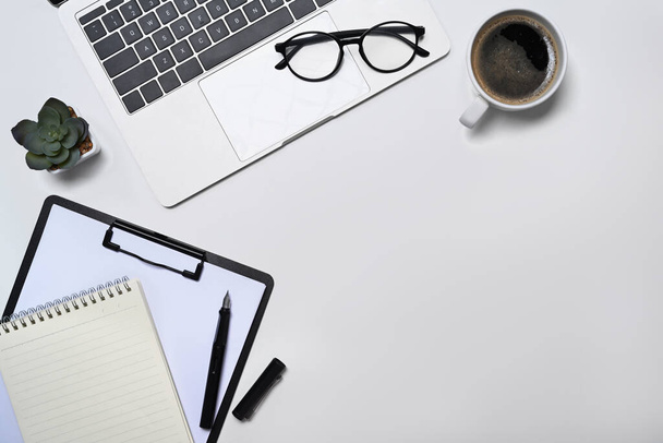 Computador portátil, óculos, xícara de café, notebook e planta suculenta na mesa do escritório branco. Flat lay, vista superior - Foto, Imagem