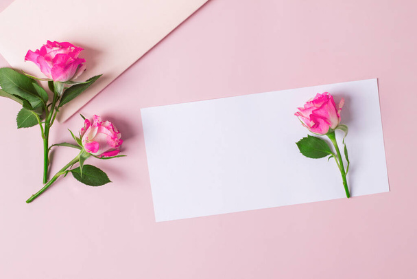 Composition with delicate pink rose flowers and blank paper on a pastel pink background. Greetind card mockup. - 写真・画像