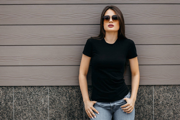 Stylová brunetka dívka v černém tričku a slunečních brýlích pózující proti ulici, městský styl oblečení. Pouliční fotografie - Fotografie, Obrázek