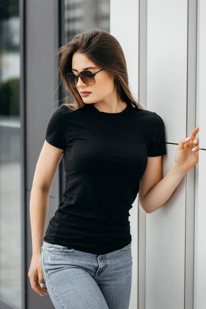 Stylish brunette girl wearing black t-shirt and sunglasses posing against street , urban clothing style. Street photography - Фото, зображення