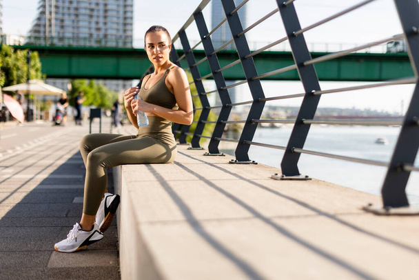 Pretty young woman taking a break during exercise on the river promenade - 写真・画像