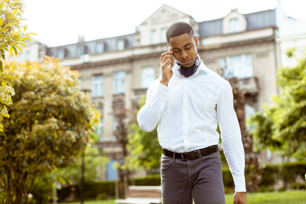 Handsome young African American businessman using a mobile phone while walking on a street - Fotoğraf, Görsel