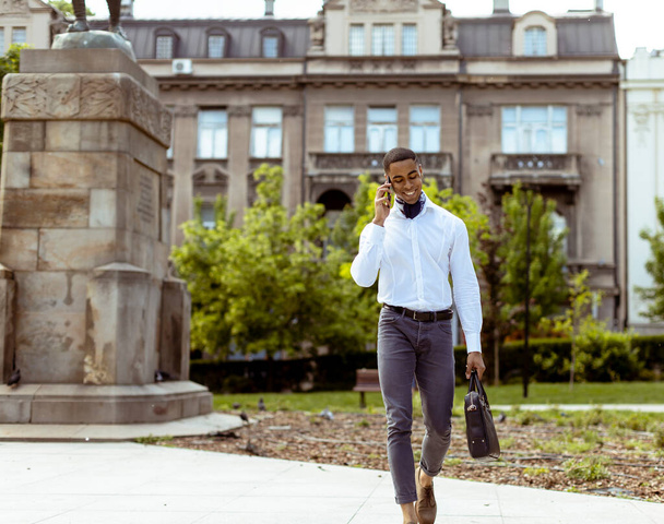 Handsome young African American businessman using a mobile phone while walking on a street - Foto, Imagem