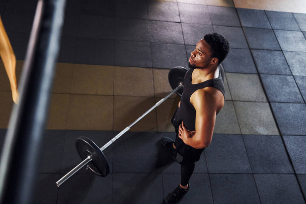 Top view. Barbell on the floor. Strong african american man in sportive clothes have workout day in the gym. - Fotoğraf, Görsel