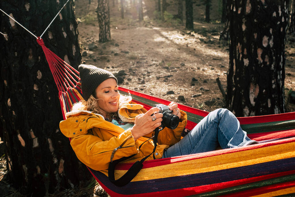 写真カメラを持つ美しい若い大人の女性は、屋外の野生の森の中でハンモックに乗って旅行活動を楽しむ-代替冒険休暇だけで公園で陽気な女性の人々 - 写真・画像