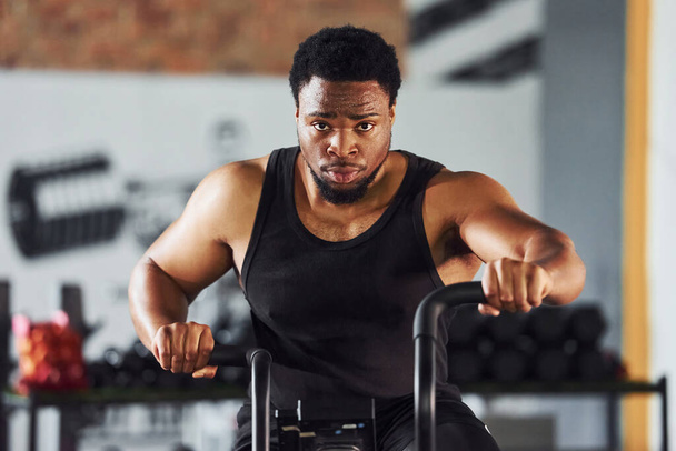 Forte uomo afro-americano in abiti sportivi hanno giornata di allenamento in palestra utilizzando attrezzature. - Foto, immagini