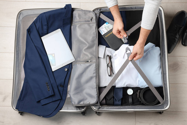 Man packing suitcase for business trip on wooden floor, top view - Fotó, kép
