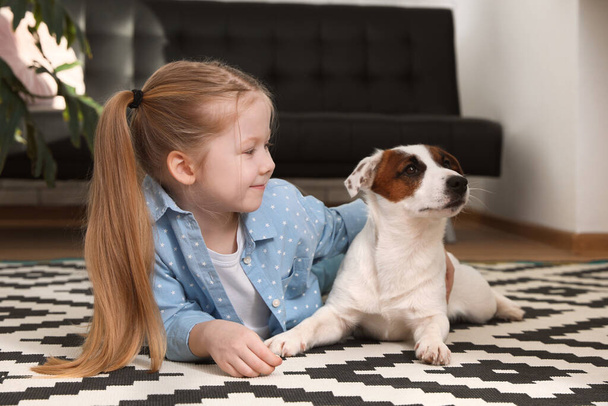 Cute little girl with her dog on carpet at home. Childhood pet - 写真・画像