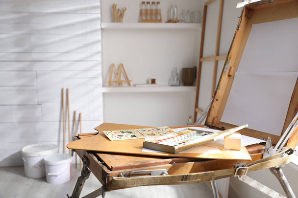 Cavalletto pieghevole in legno con tela vuota e forniture in studio. Luogo di lavoro dell'artista - Foto, immagini