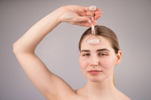 Close-up retrato de uma mulher usa um massageador de rolo de quartzo para suavizar rugas na testa. - Foto, Imagem
