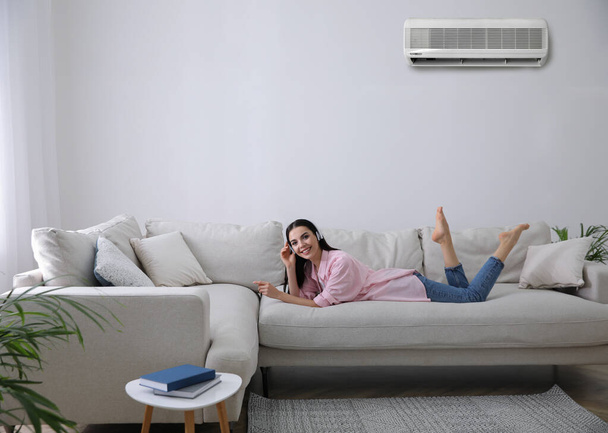 Young woman resting under air conditioner on white wall at home - Fotografie, Obrázek