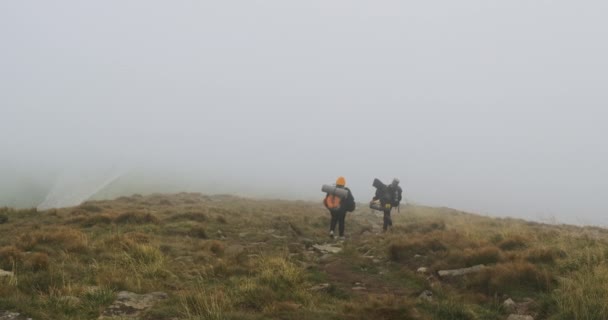 chlapík a dívka jsou turisté, s velkými těžkými batohy, sestupující z hory pokryté hustou mlhou. Špatné počasí, mraky. - Záběry, video